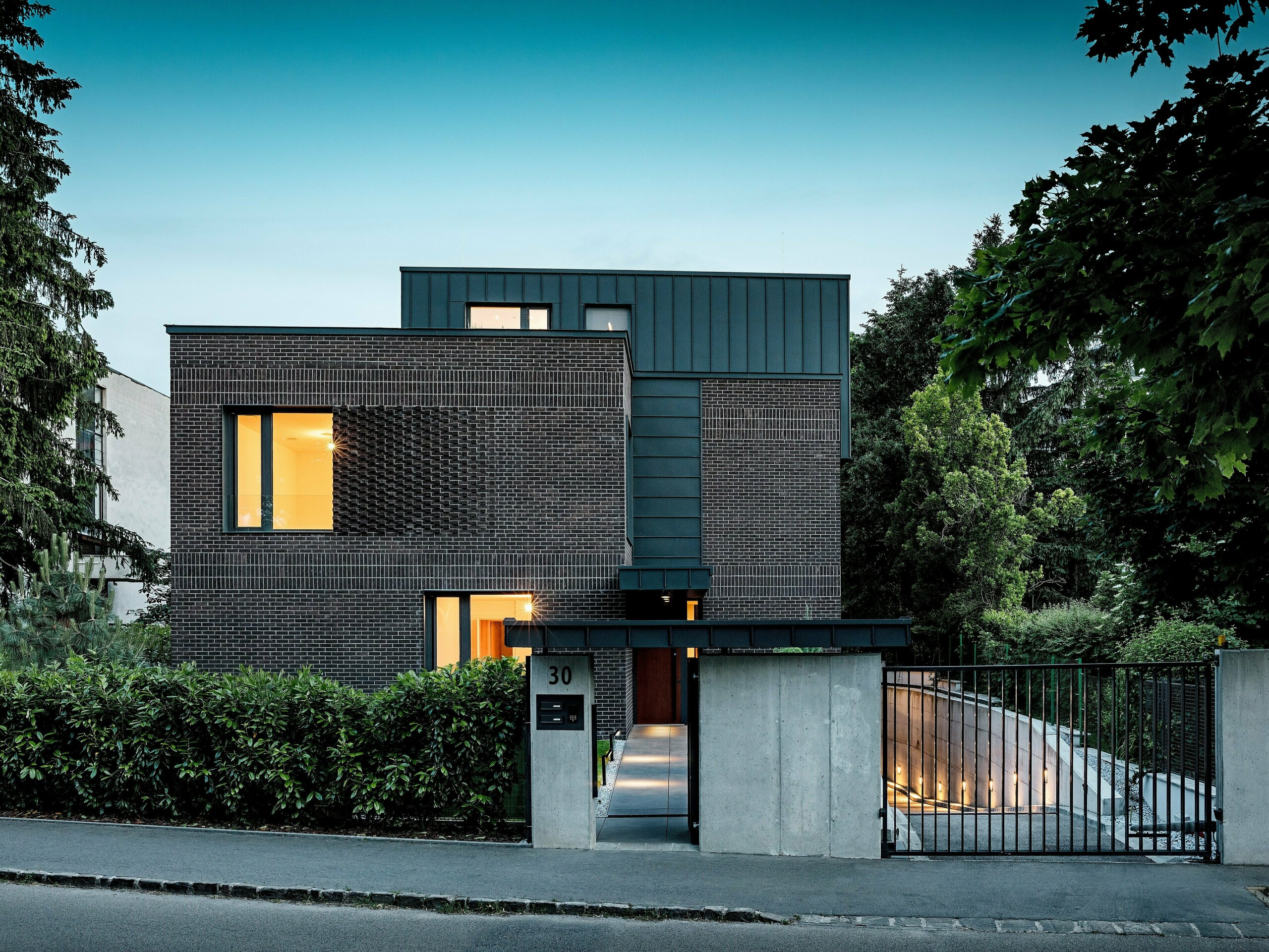 Das Bild zeigt ein modernes Mehrfamilienhaus in Budapest, dessen kubischer Dachaufbau mit PREFALZ Aluminium in P.10 Anthrazit einen markanten Kontrast zur historischen Umgebung bildet. Die vertikalen Winkelstehfalze erzeugen ein spannendes Lichtspiel und betonen die klare Architektursprache. Die hochwertigen PREFA Aluminiumprodukte verleihen dem Gebäude nicht nur eine elegante, zeitlose Optik, sondern überzeugen durch Langlebigkeit, Witterungsbeständigkeit und präzise Verarbeitung. Der anthrazitfarbene Fassaden- und Dachbereich fungiert als kraftvoller Eyecatcher und unterstreicht den innovativen Charakter des Bauwerks.