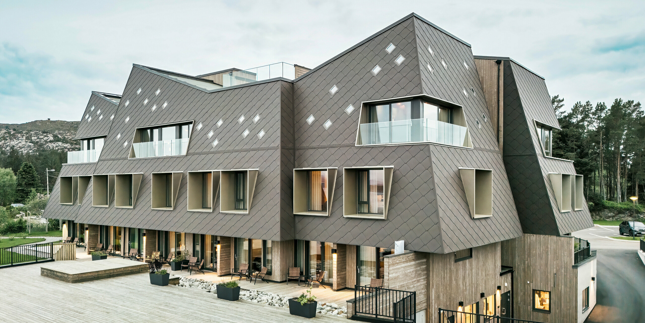 Utsikt over terrassen på hotellet Beckerwyc House i Bekkjarvik, Norge. Den moderne bygningen er utsmykket med en iøynefallende aluminiumsfasade laget av PREFA-veggribber 44 × 44 i valnøttbrun. Den futuristiske arkitekturen med skrånende takflater og utstikkende vinduselementer kompletteres av de romslige uteområdene. Fasadens naturlige farge passer harmonisk inn i det omkringliggende landskapet og understreker bygningens moderne design.