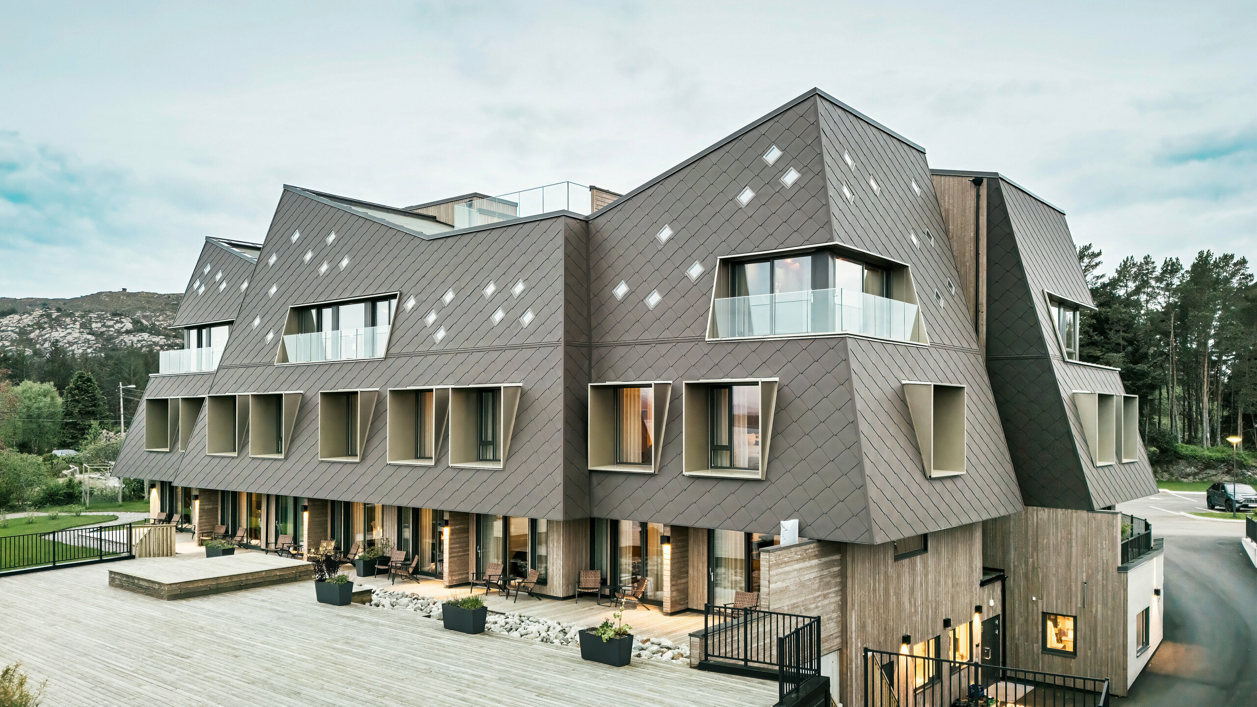 Utsikt over terrassen på hotellet Beckerwyc House i Bekkjarvik, Norge. Den moderne bygningen er utsmykket med en iøynefallende aluminiumsfasade laget av PREFA-veggribber 44 × 44 i valnøttbrun. Den futuristiske arkitekturen med skrånende takflater og utstikkende vinduselementer kompletteres av de romslige uteområdene. Fasadens naturlige farge passer harmonisk inn i det omkringliggende landskapet og understreker bygningens moderne design.