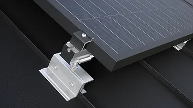 Nærbilde av PREVARIO PREFALZ holder for solcellepanel, montert på et mørkt PREFA-tak som bærer profilskinnen. Solcellemodulen ble feste til profilskinnen med PREVARIO-endeklemmen.