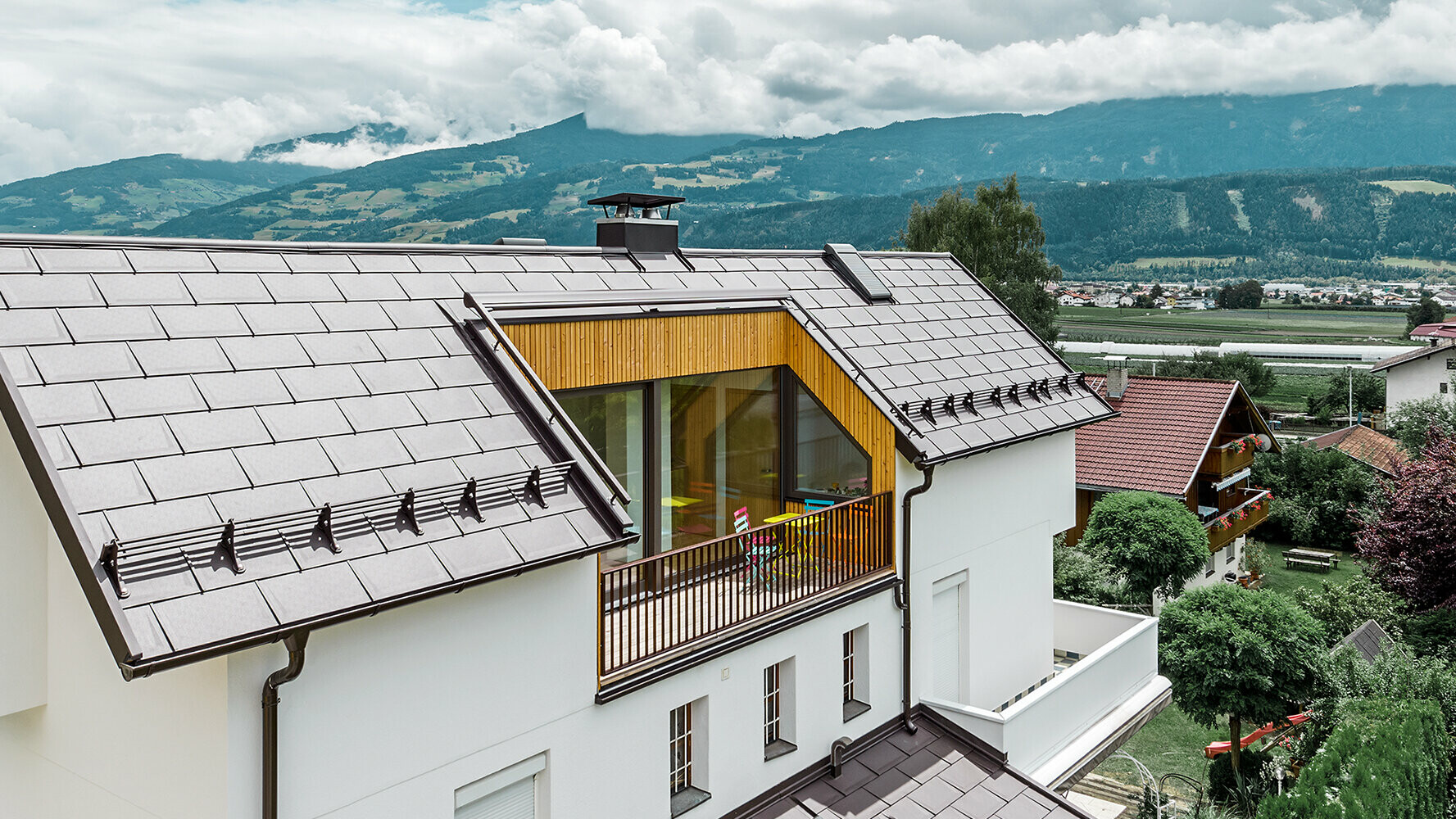 Bolighus tekket med takplater R.16 i nøttebrunt aluminium fra PREFA. Huset har en stor balkong og lys pusset fasade.