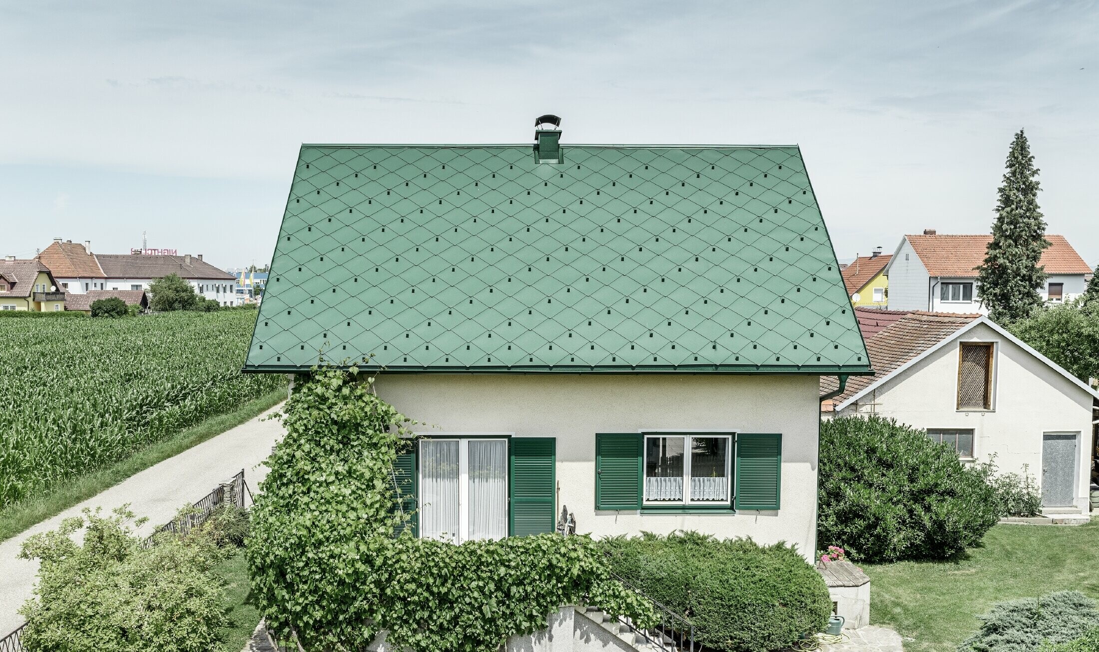 Klassisk enebolig med saltak og takkledning i mosegrønn aluminium med grønne vinduskodder. Taket er tekket med PREFA takrombe 44 × 44 i P.10 mosegrønt.