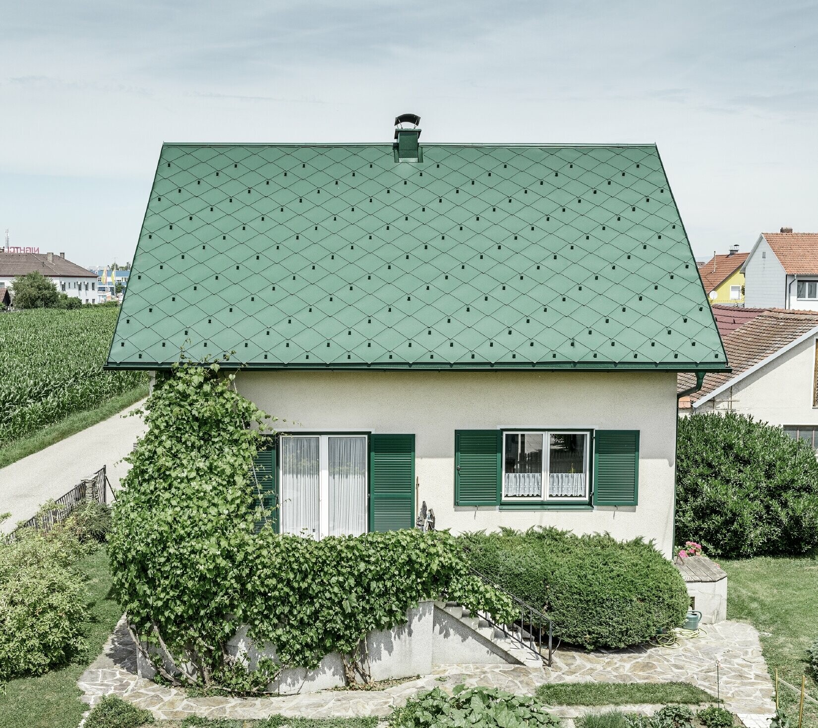 Klassisk enebolig med saltak og takkledning i mosegrønn aluminium med grønne vinduskodder. Taket er tekket med PREFA takrombe 44 × 44 i P.10 mosegrønt.