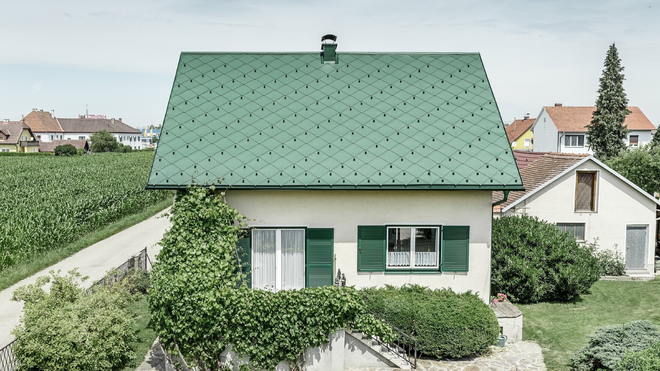 Klassisk enebolig med saltak og takkledning i mosegrønn aluminium med grønne vinduskodder. Taket er tekket med PREFA takrombe 44 × 44 i P.10 mosegrønt.