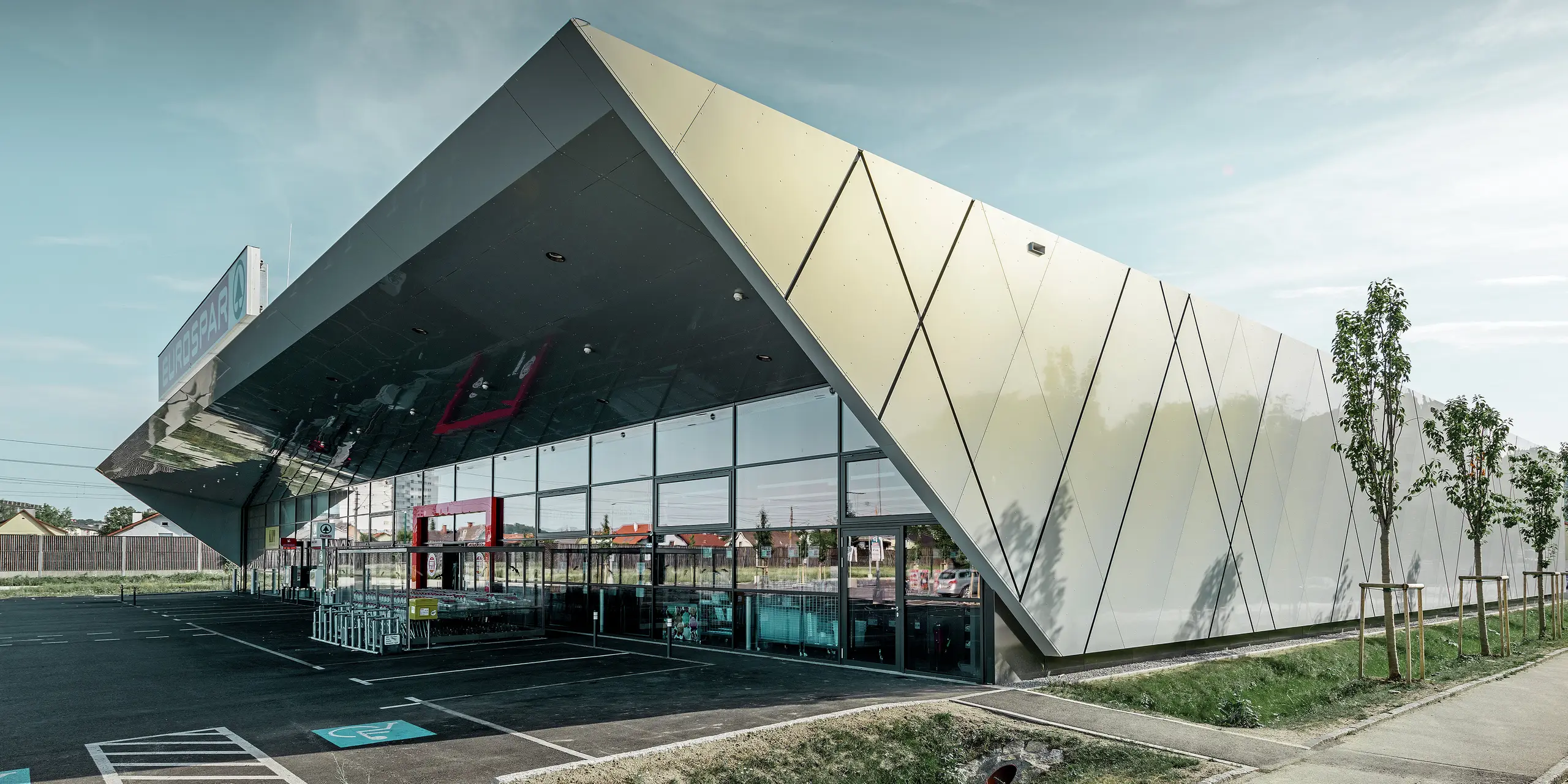 Inngangspartiet til den nye Eurospar filialen i Wels med den moderne fasadeplaten fra PREFA i sølv og gull. Aluminiumskomposittplatene funkler i solen i forskjellige farger alt etter fra hvilken vinkel man ser.