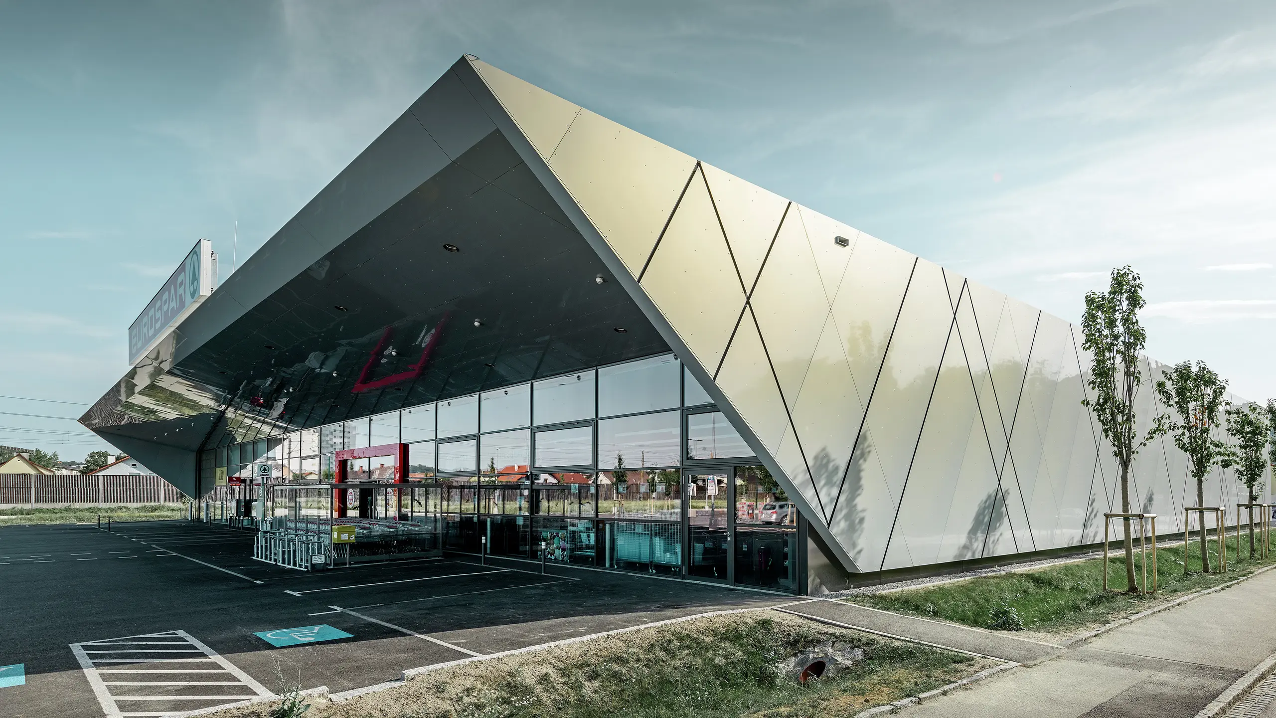 Inngangspartiet til den nye Eurospar filialen i Wels med den moderne fasadeplaten fra PREFA i sølv og gull. Aluminiumskomposittplatene funkler i solen i forskjellige farger alt etter fra hvilken vinkel man ser.