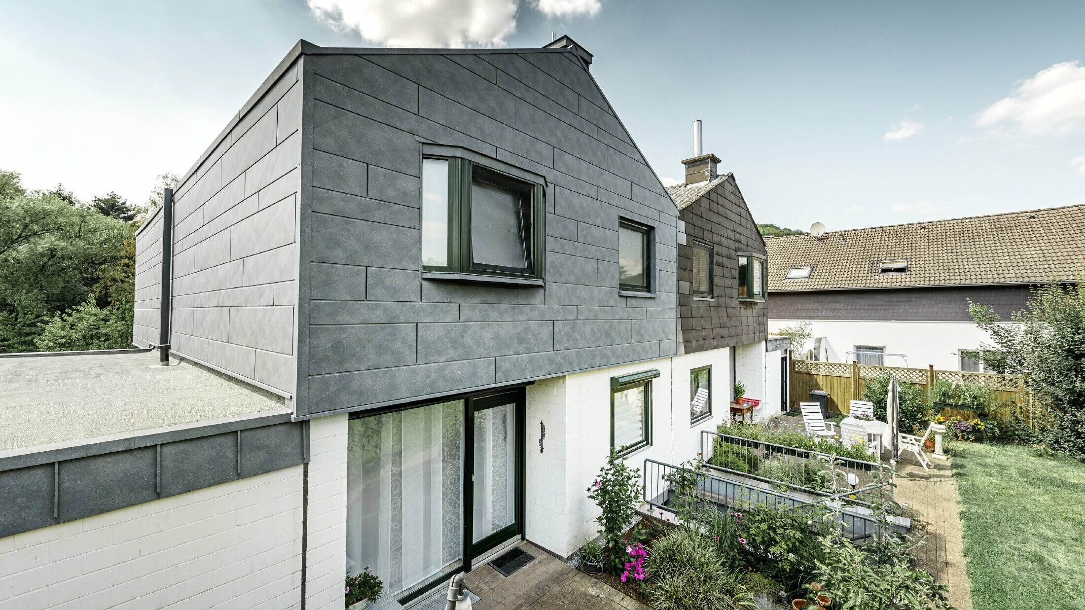 Den øverste delen av tomannsboligen er renovert med PREFA fasadeelement Siding.X i P.10 steingrå. Til sammenligning rett ved siden av tomannsboligen før renoveringen.