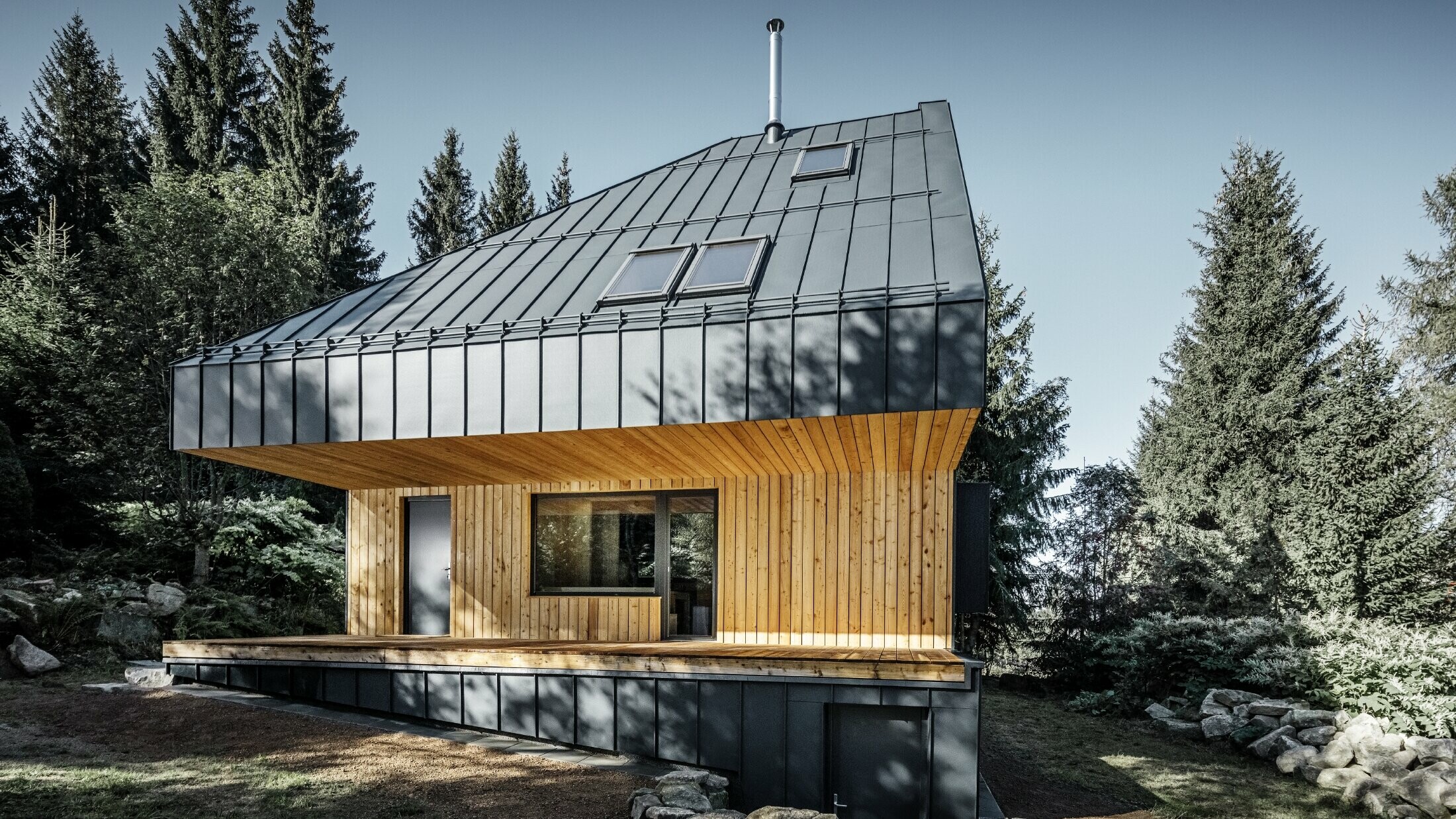 Arkitektonisk enebolig i skogen, det imponerende taket ble kledd medPrefalz i antrasitt. Undertaket og fasaden er kledd med trepanel.