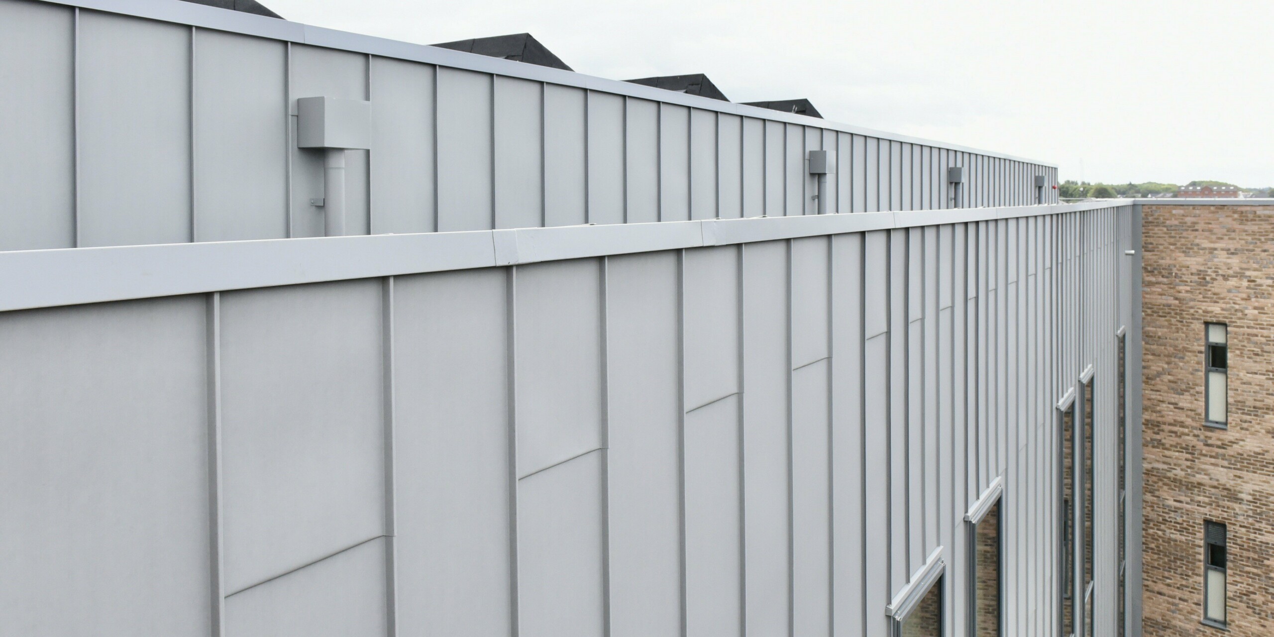 Detailansicht der PREFALZ Aluminiumfassade in Patinagrau am Regional College North, UK. Die klare Linienführung und die matte Optik der Stehfalzverkleidung unterstreichen die hochwertige Verarbeitung und das zeitlose Design.