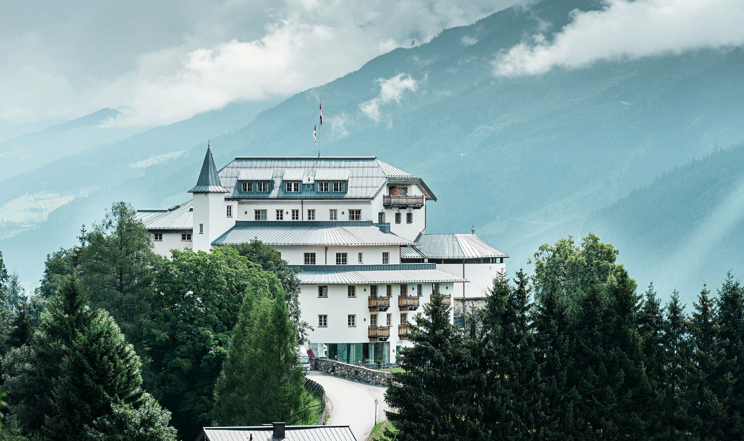 Schloss Mittersill umgeben von Bäumen und Bergen mit einem neu sanierten Prefalz Dach in steingrau