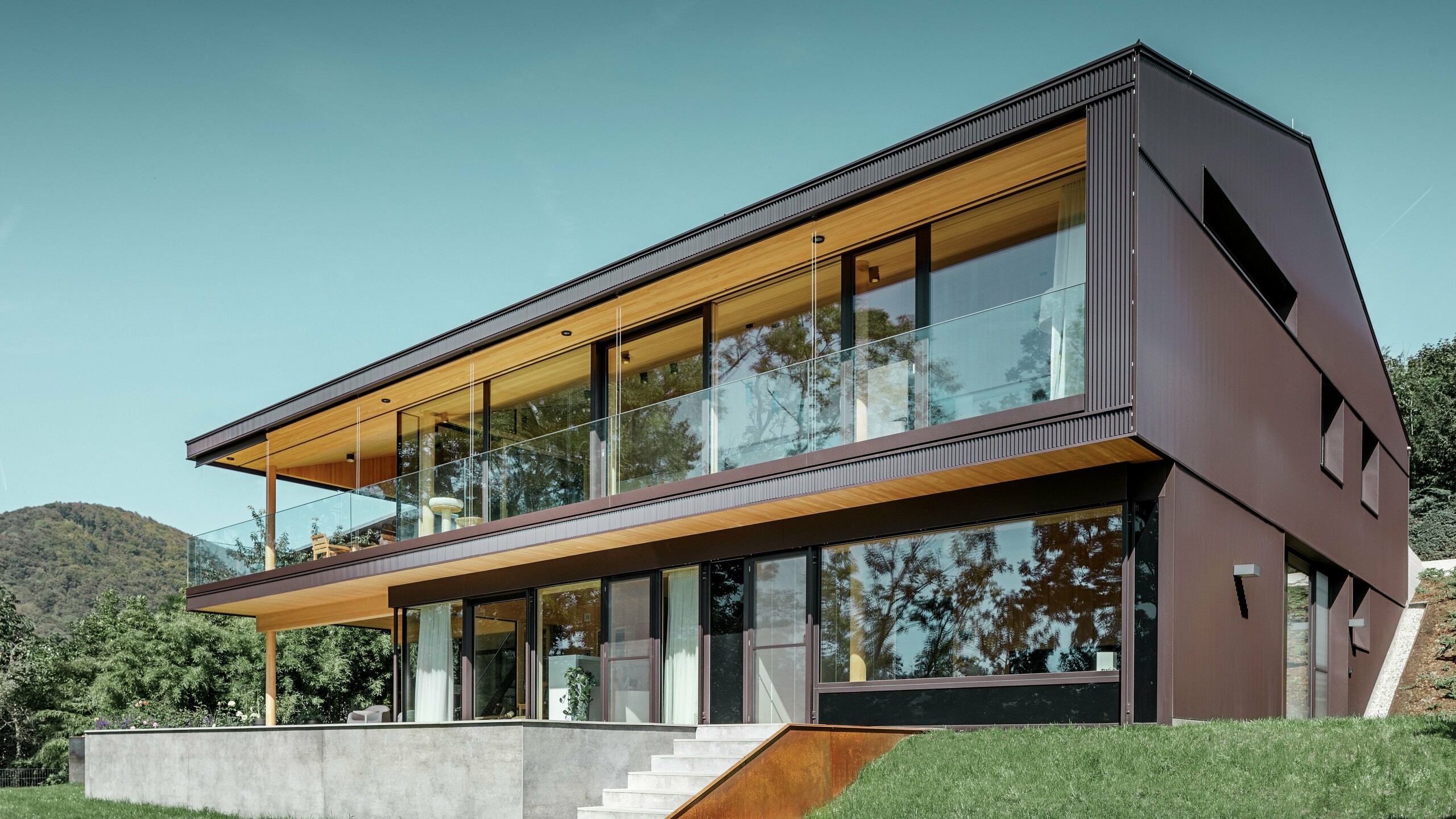 Moderne enebolig med store vinduer på hagesiden, fasaden er kledd med PREFA sikksakkprofil i mørkebrunt.