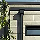 Moderne enebolig med flatt tak og smale vinduer. Fasaden er kledd med PREFA Siding.X-fasade med foldet utseende i fargen bronse. Forbindelsene ble laget i antrasitt. PREFA firkantrør med tilhørende vannoppsamlingsbeholder i antrasitt brukes til takdrenering.