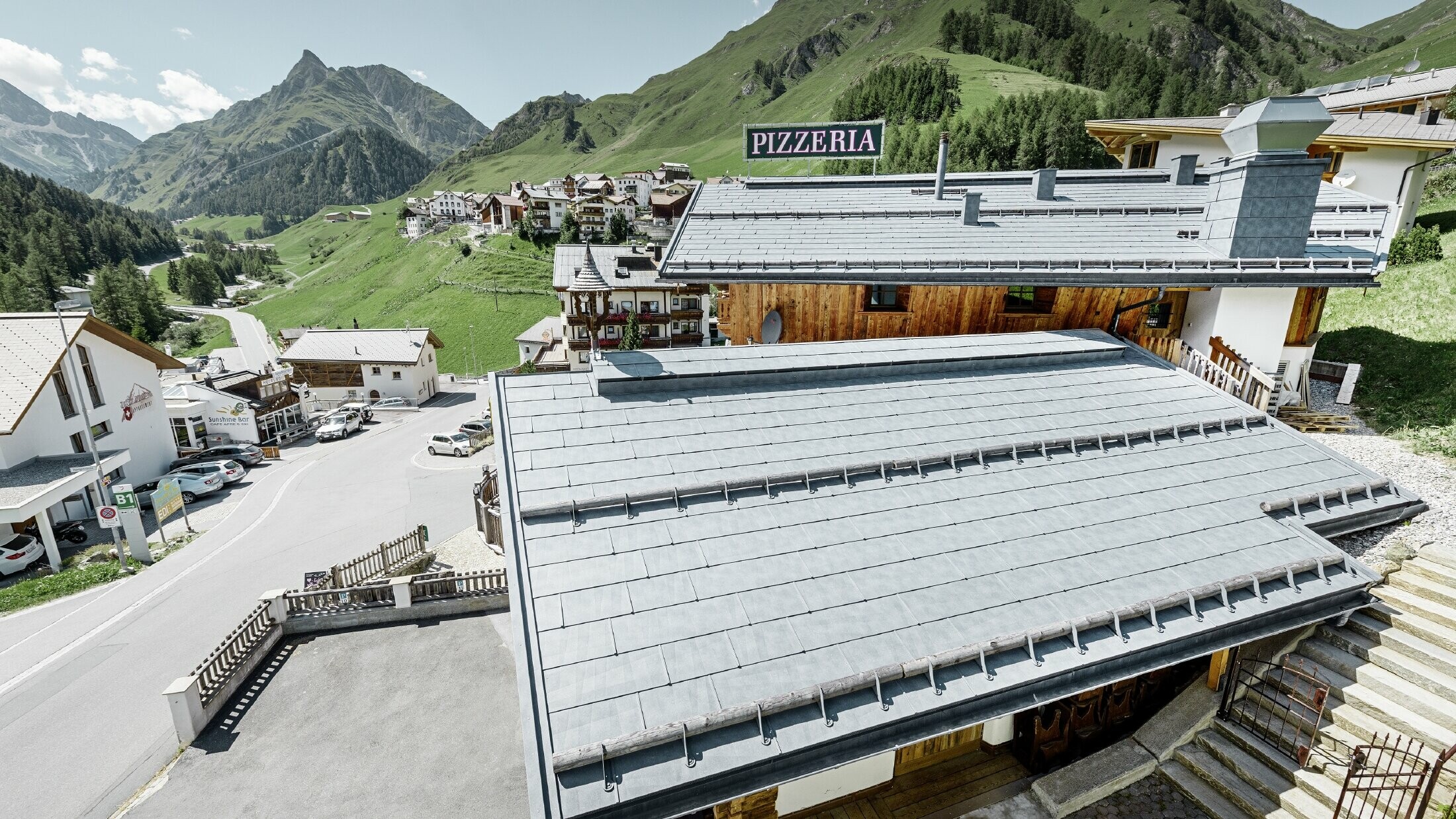 Almrausch-restaurant med fjell i bakgrunnen og et PREFA-tak med FX.12 takpanel i steingrå og fjellsnøstøtter.
