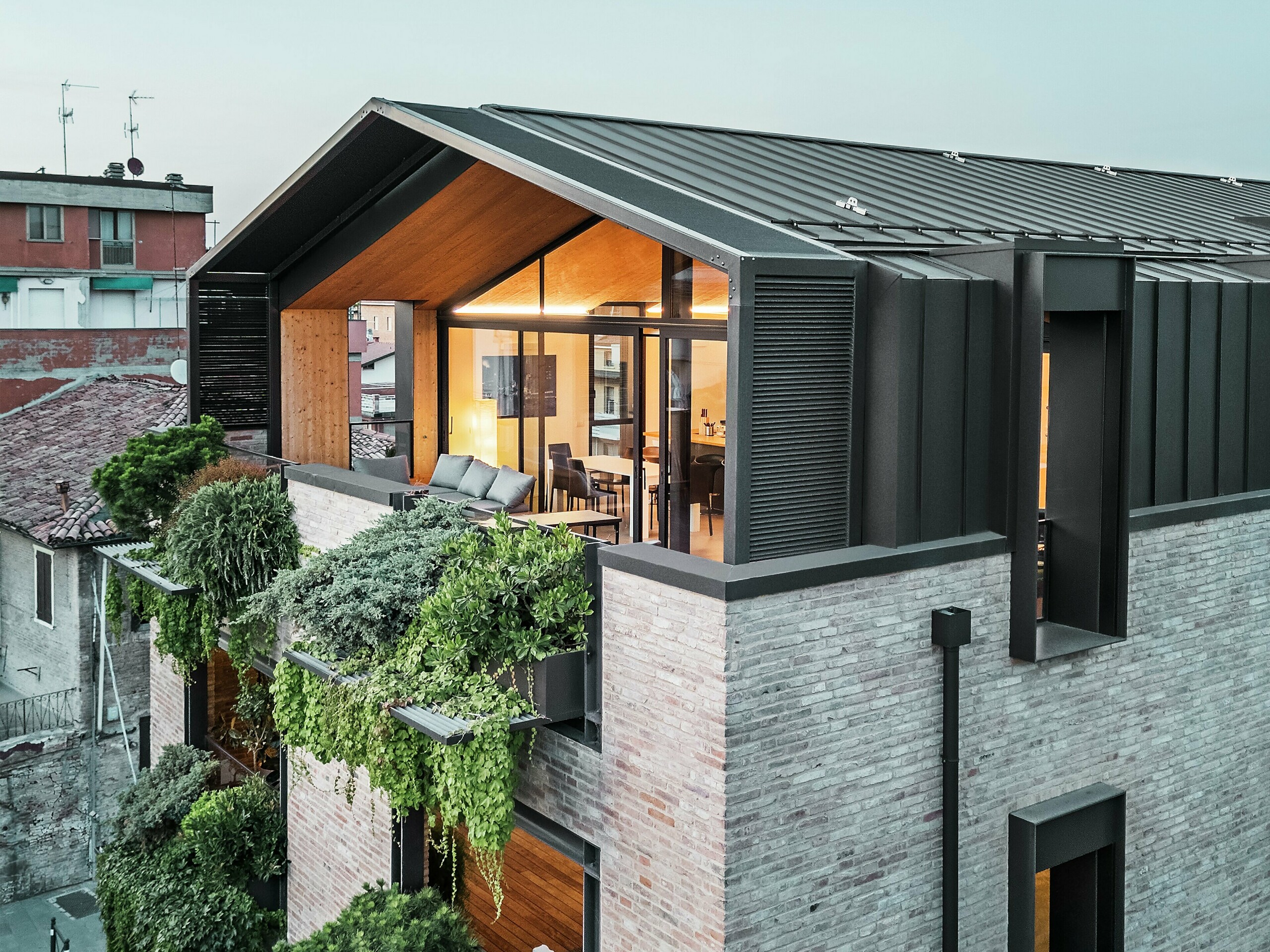 Ein modernes Wohnhaus in Italien mit einem PREFALZ-Aluminiumdach in der Farbe P.10 Haselnussbraun, großen Glasflächen, einer grünen Fassade und Ziegeln - eine gelungene Kombination aus Nachhaltigkeit und zeitgenössischer Architektur.