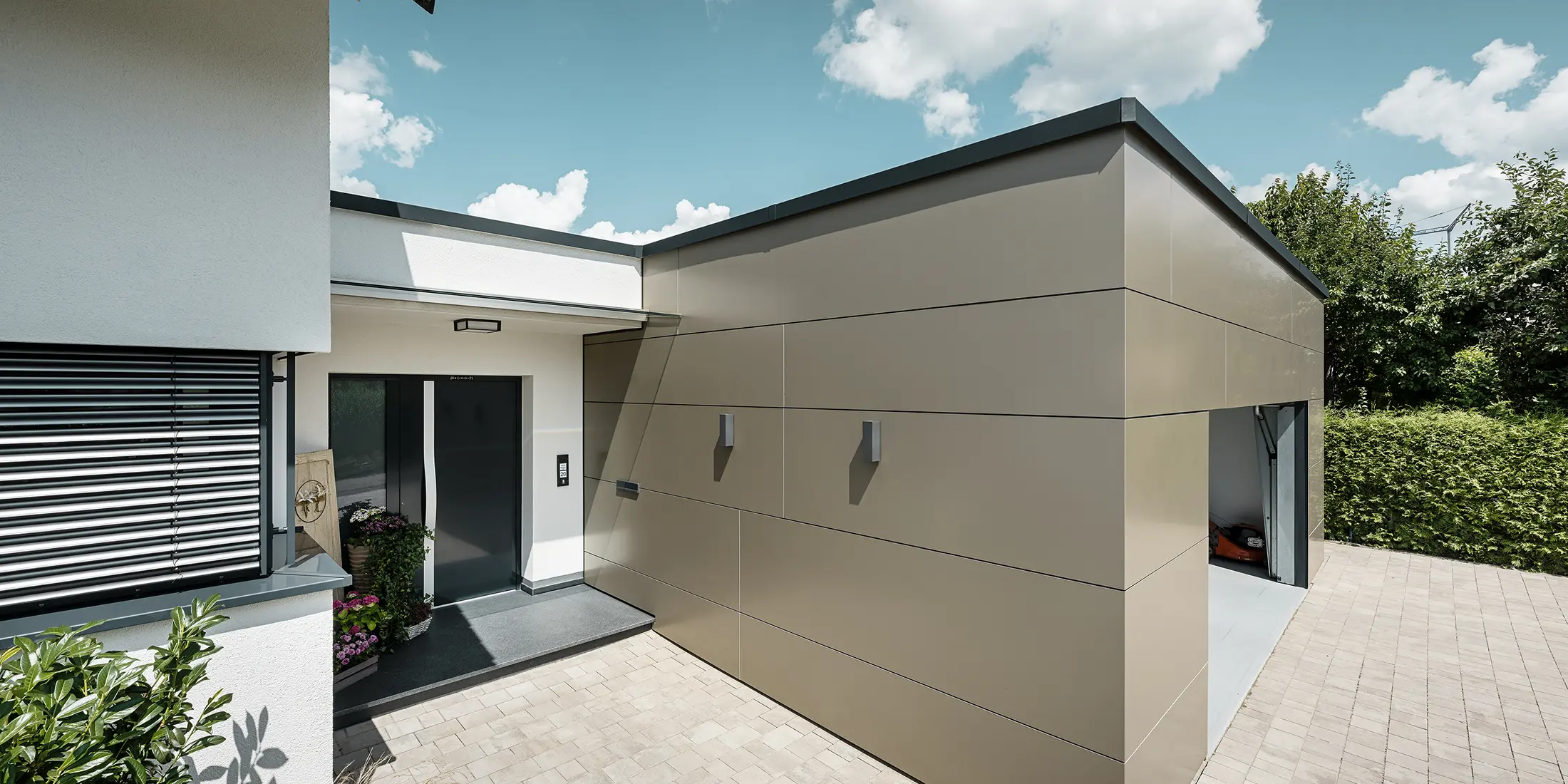 Seitliche Ansicht einer Garage mit PREFABOND Aluminium Verbundplatten in Bronze an der Fassade. Man sieht auch den Eingangsbereich des Hauses.