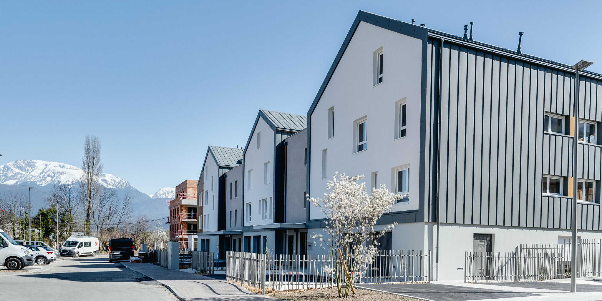 Sicht von der Straße auf die Résidence L’Athéna. Die Résidence L’Athéna besteht aus mehreren Gebäudeteilen, die mit PREFALZ in P.10 Hellgrau verkleidet wurden. Die Wohnanlage wurde von ARCANE Architectes in Varces-Allières-et-Risset, Freankreich errichtet.
