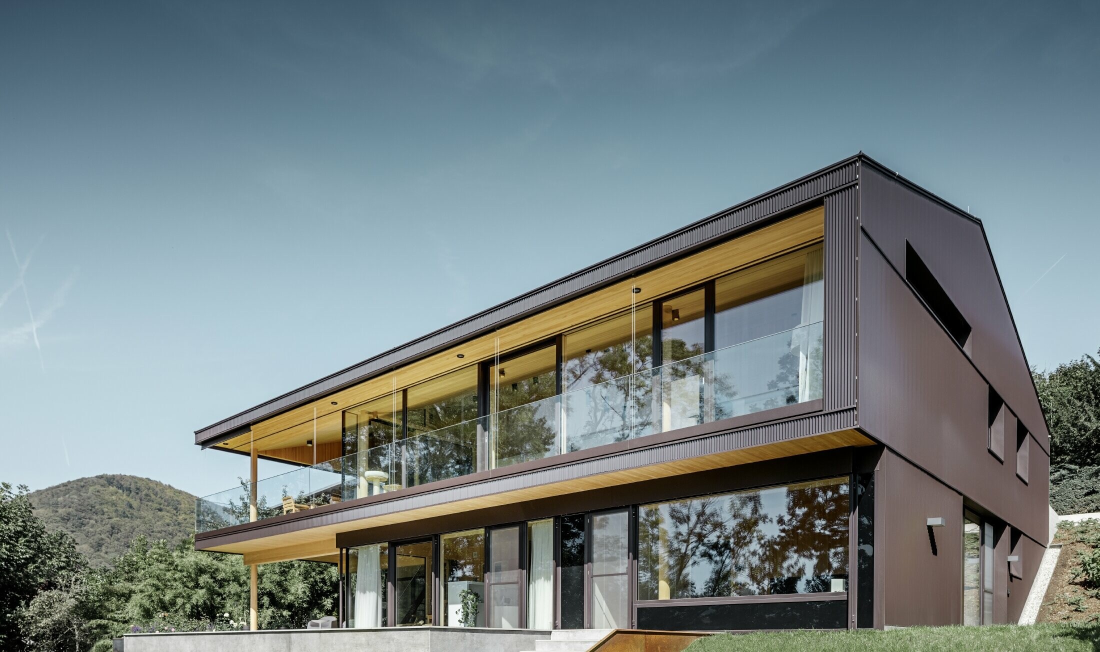 Moderne enebolig med store vinduer på hagesiden, fasaden er kledd med PREFA sikksakkprofil i mørkebrunt.