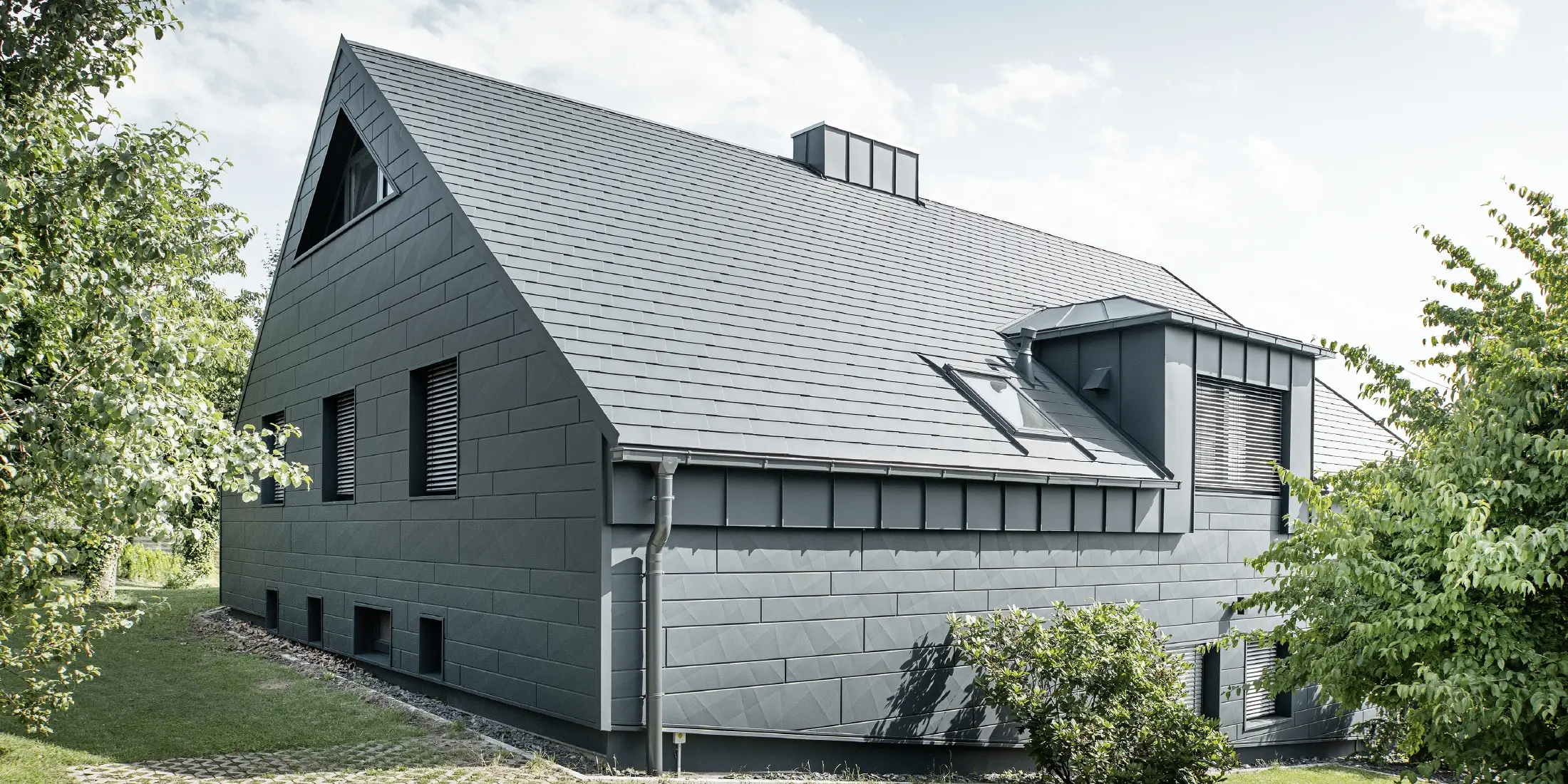 Stor enebolig med sadeltak og mange vinduer. Hele huset er kledd med en aluminiumsbekledning i antrasitt, på taket er det brukt PREFA aluminiums takspon og på fasaden Siding.X i antrasitt.