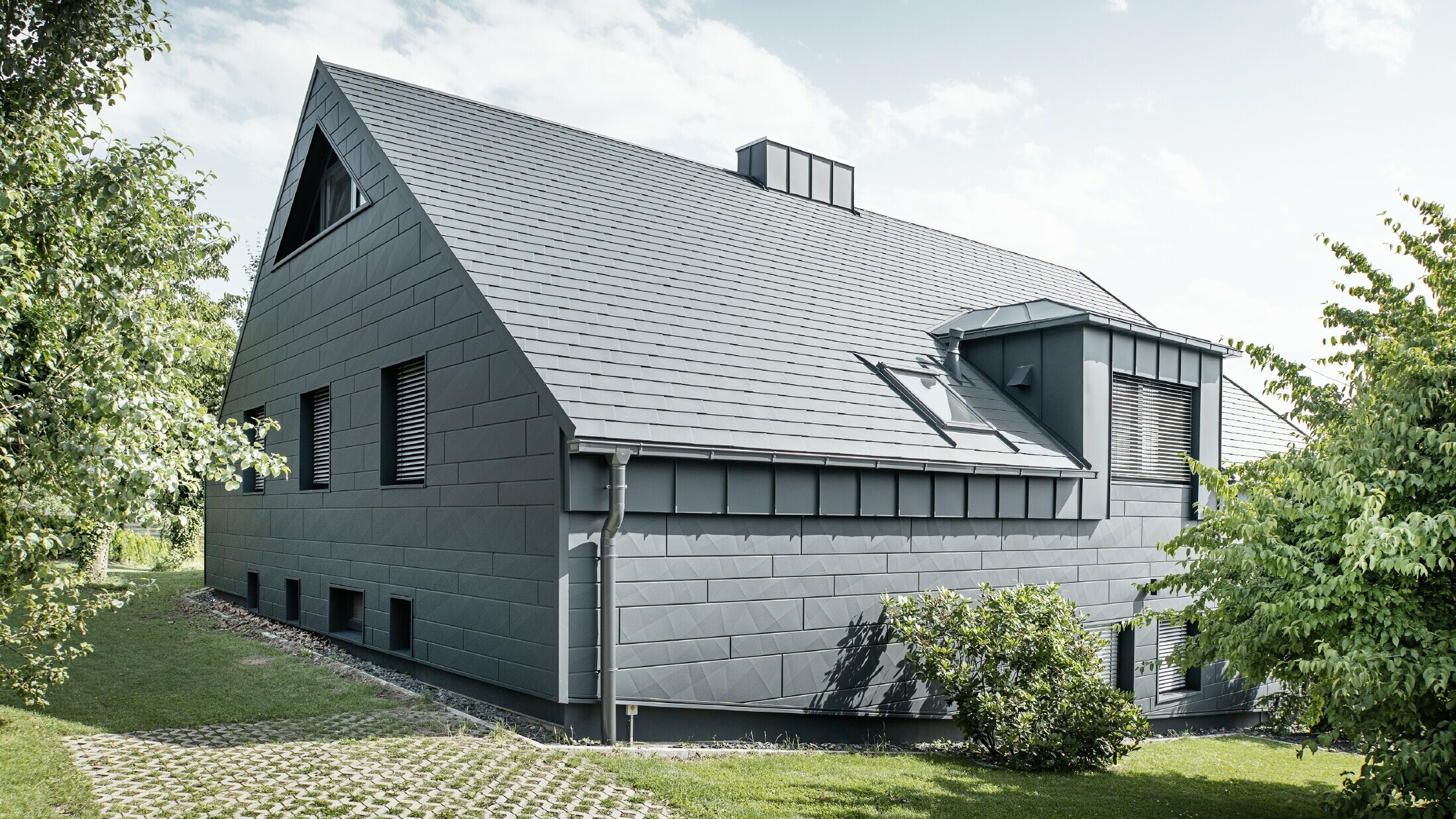 Stor enebolig med sadeltak og mange vinduer. Hele huset er kledd med en aluminiumsbekledning i antrasitt, på taket er det brukt PREFA aluminiums takspon og på fasaden Siding.X i antrasitt.