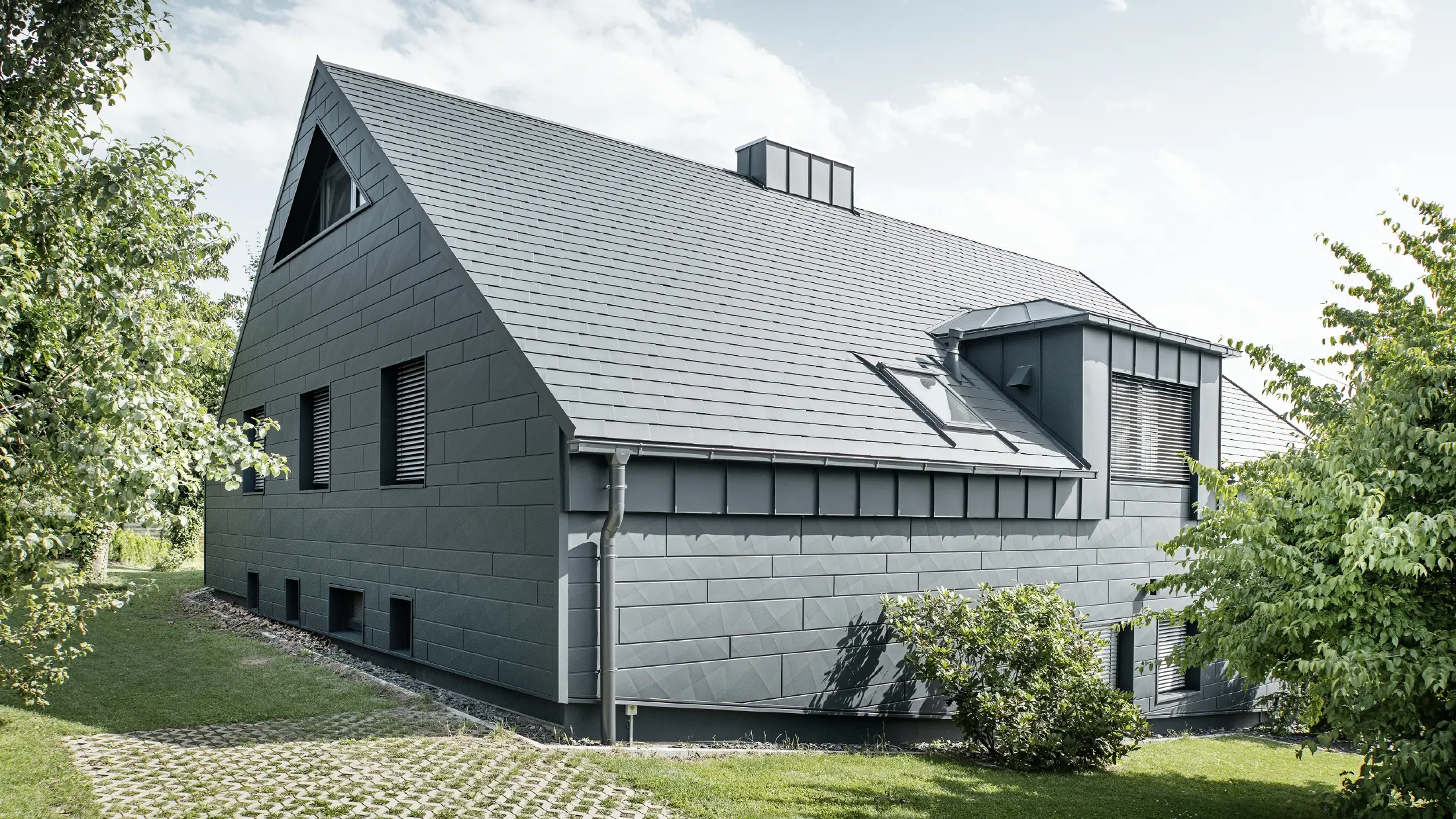 Stor enebolig med sadeltak og mange vinduer. Hele huset er kledd med en aluminiumsbekledning i antrasitt, på taket er det brukt PREFA aluminiums takspon og på fasaden Siding.X i antrasitt.