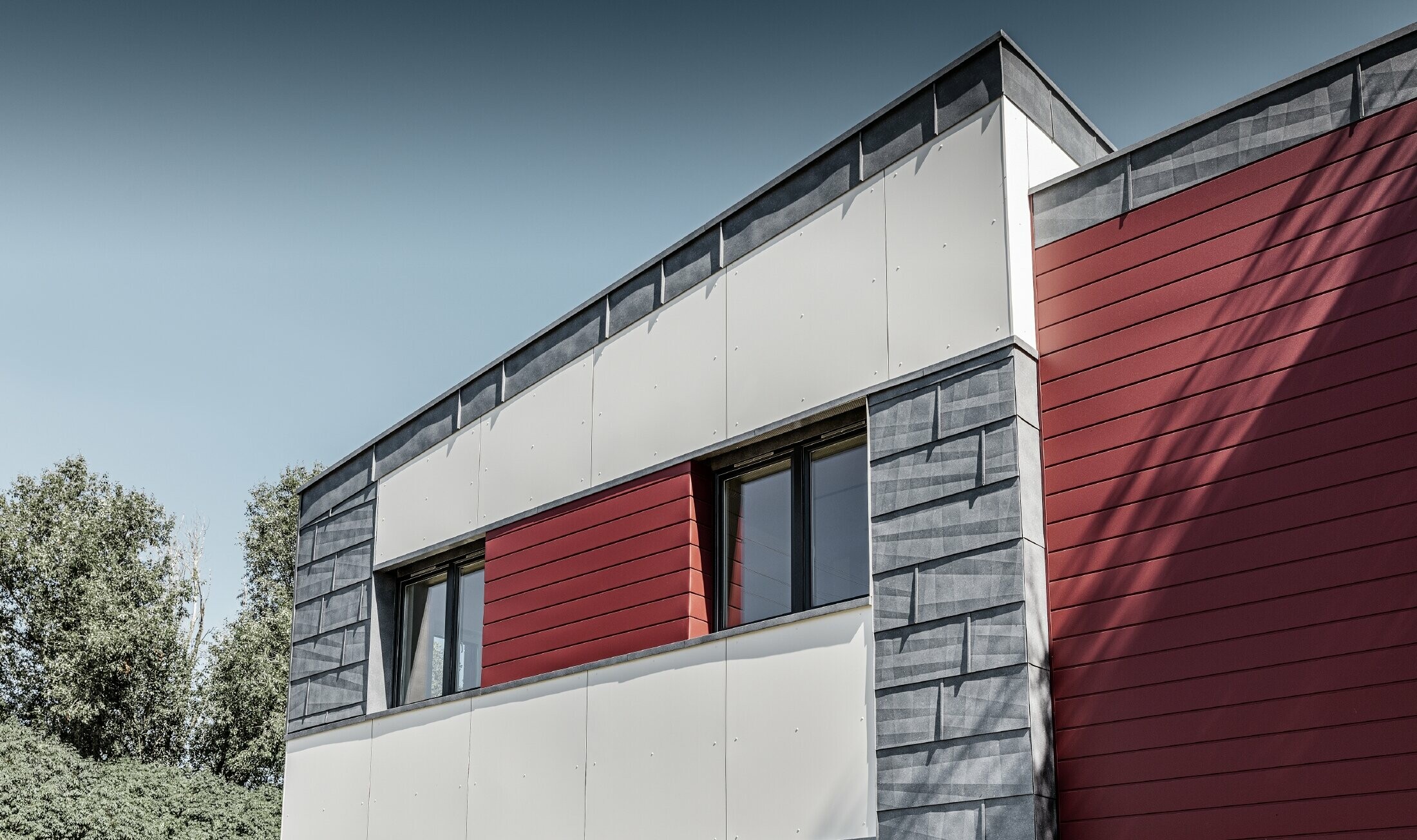 Modernes Bürogebäude mit einer geteilten Fassade in rot, steingrau und weiß mit Aluminiumprodukten Sidings, Fassadenpaneel FX.12 und Aluminium Verbundplatte von PREFA