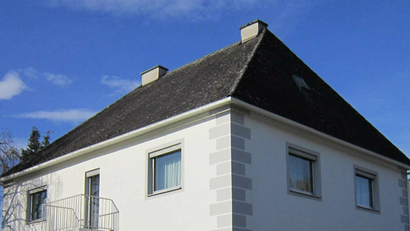 Hus med valmtak før renovering av taket med Prefalz og PREFA takplate i Østerrike