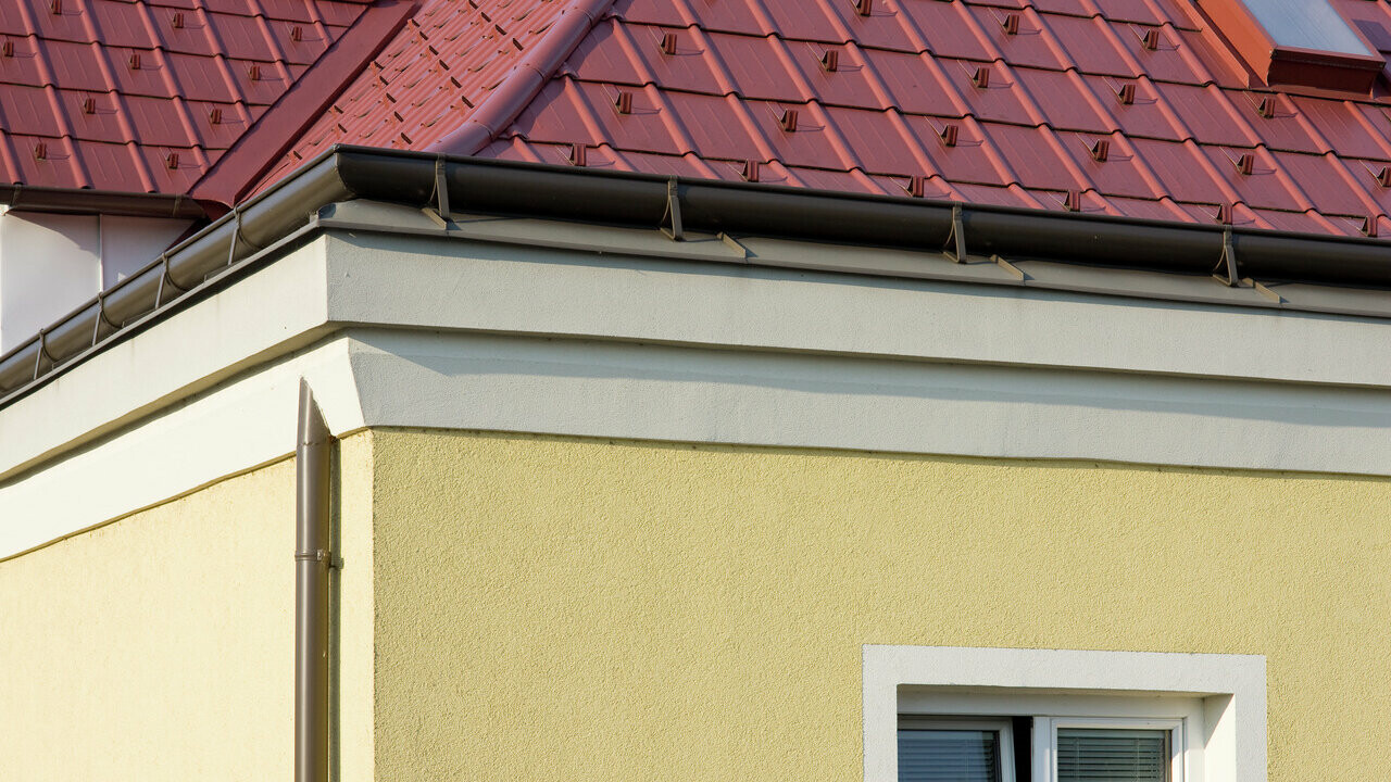 Hushjørne med gul pusset fasade og brun PREFA fotrenne med rødt PREFA takplatetak.