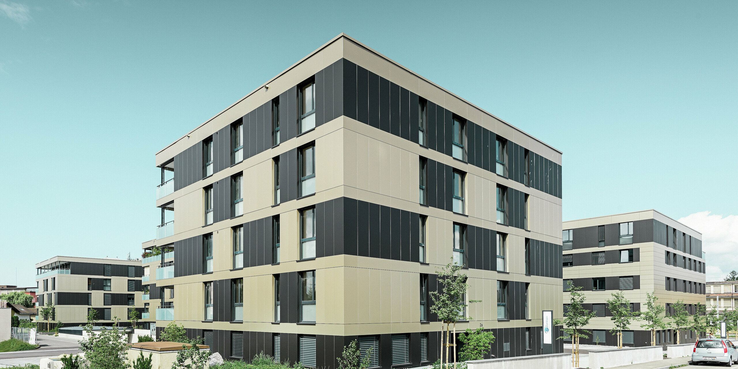 Die moderne Architektur dieser Wohnanlage in Murten (CH) wird durch die PREFA Fassade mit Aluminium Verbundplatten in Bronze und Schwarzgrau unterstrichen. Die langlebige und pflegeleichte Oberfläche schützt das Gebäude nicht nur vor Umwelteinflüssen, sondern verleiht dem gesamten Baukörper ein elegantes und zeitloses Design.