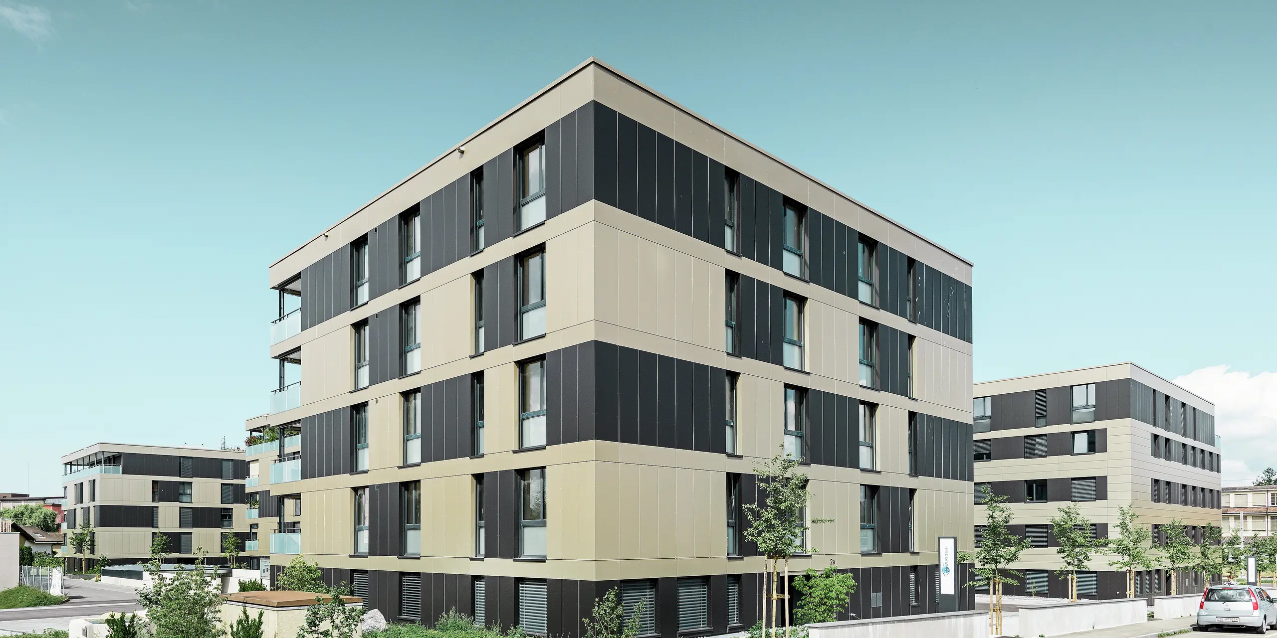 Die moderne Architektur dieser Wohnanlage in Murten (CH) wird durch die PREFA Fassade mit Aluminium Verbundplatten in Bronze und Schwarzgrau unterstrichen. Die langlebige und pflegeleichte Oberfläche schützt das Gebäude nicht nur vor Umwelteinflüssen, sondern verleiht dem gesamten Baukörper ein elegantes und zeitloses Design.