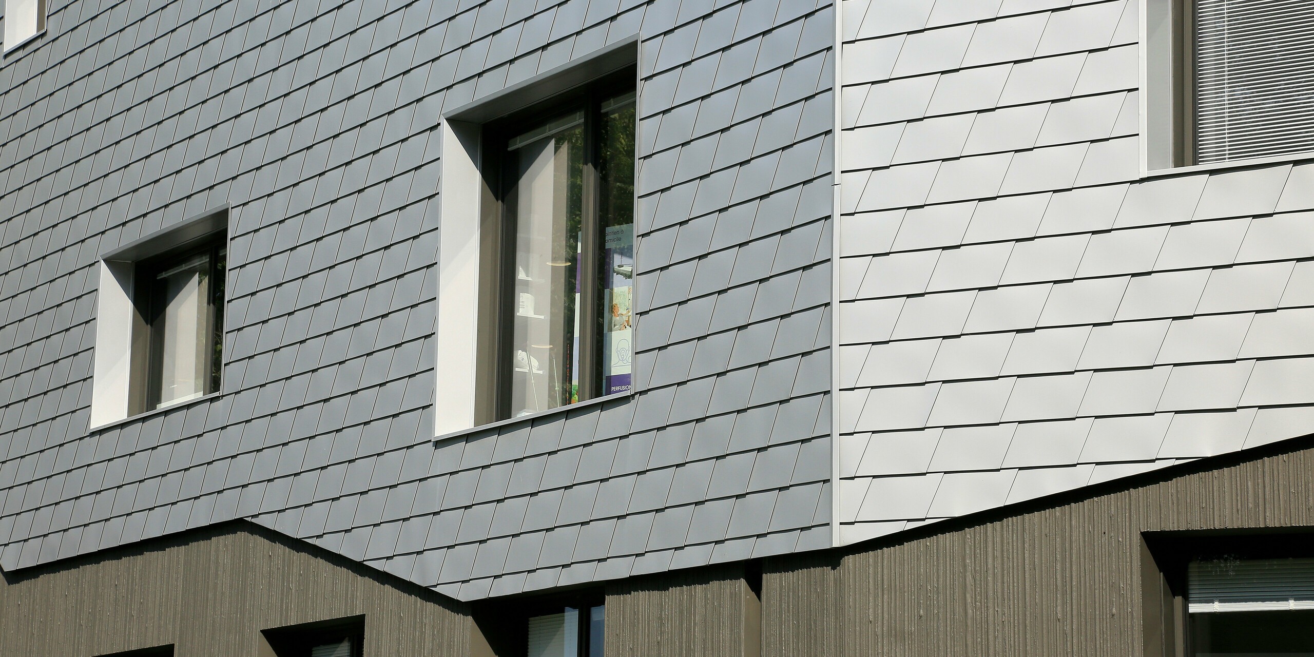 Detailansicht der Fassade des Gesundheitszentrums in Le Landreau mit dem Übergang vom Betonsockel zu PREFA Wandschindeln in Silbermetallic