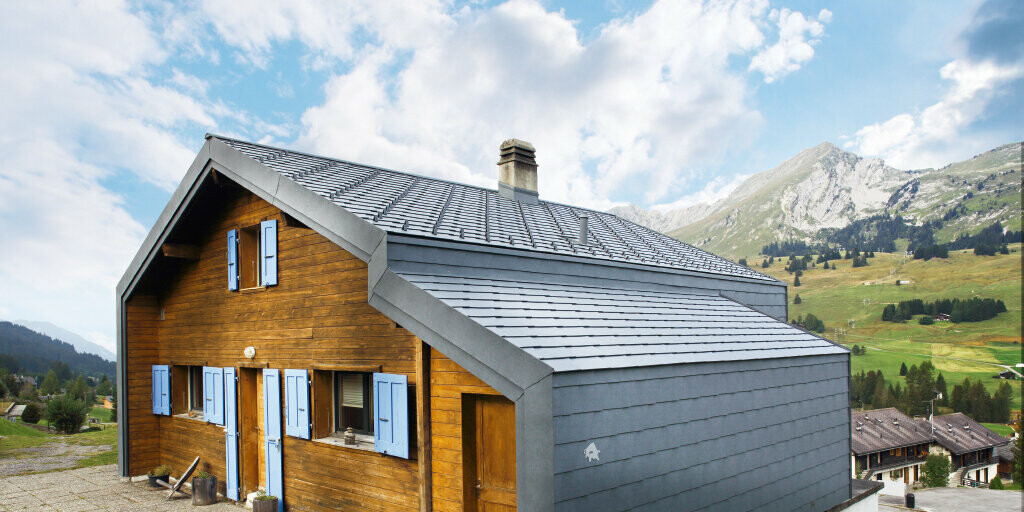 Hus i de sveitsiske fjellene med trefasade i kombinasjon med PREFA tak- og veggromber i steingrått