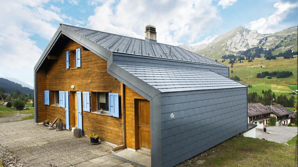 Hus i de sveitsiske fjellene med trefasade i kombinasjon med PREFA tak- og veggromber i steingrått