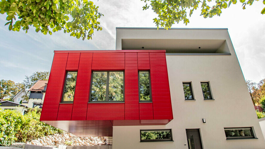 Façade moderne d'une maison individuelle avec bardage Prefa en rouge rubis, combiné à une façade beige.
