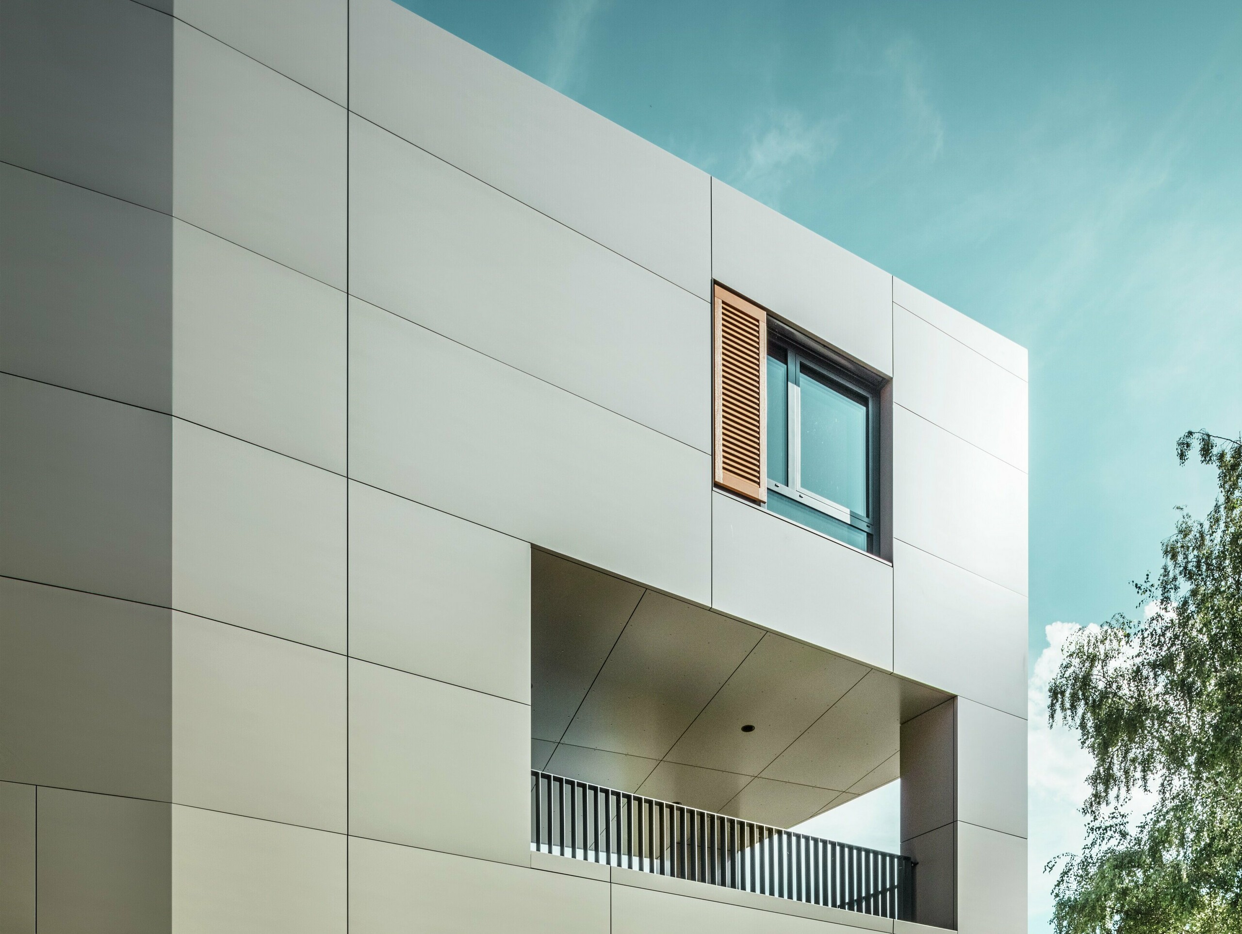 Slika prikazuje modernu gradsku vijećnicu u Alzenauu s fasadom od aluminijskih kompozitnih ploča PREFA u brončanoj boji. Arhitektura se odlikuje jasnim geometrijskim oblicima i velikim prozorima. Šiljasti krovni dio i suzdržano osvjetljenje daju zgradi elegantan, suvremen izgled.