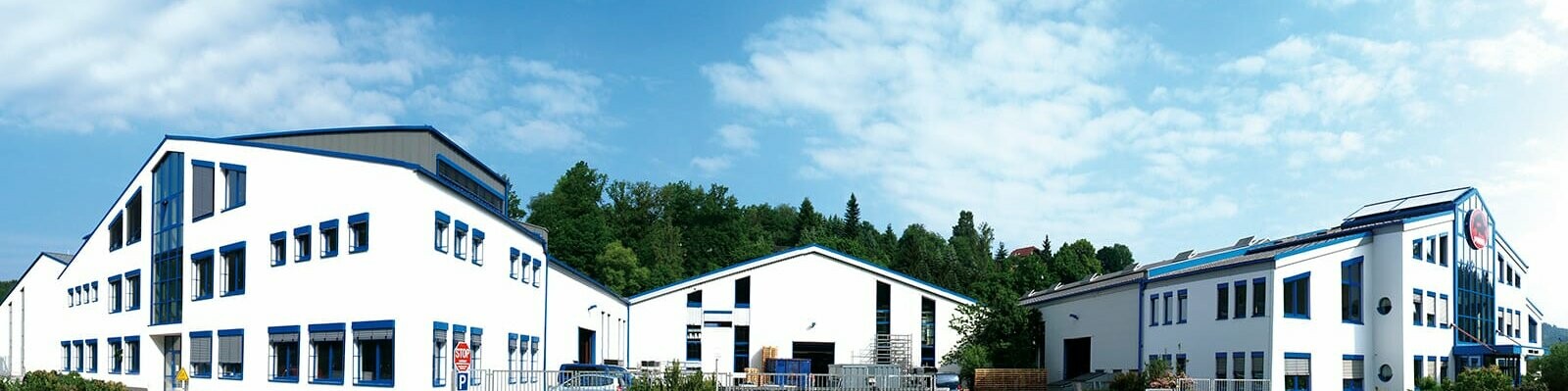 Panoramaaufnahme des PREFA Standorts in Wasungen, Deutschland; weißes Gebäude mit blauen Fenstern