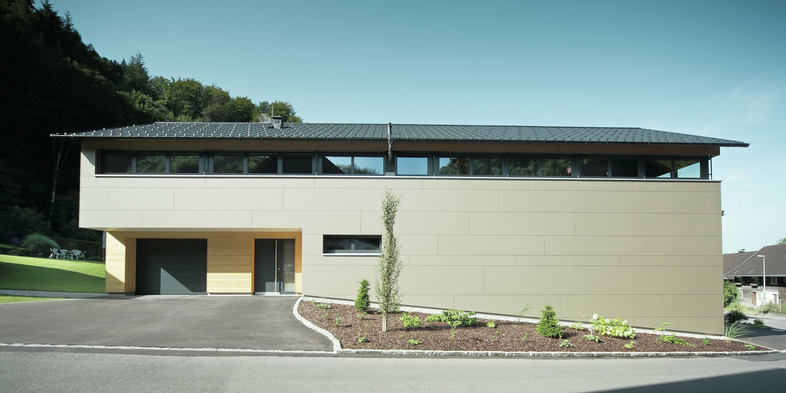 Hus med PREFA takpanel i P.10 antrasitt, kombinert med PREFA komposittpanel i bronse på fasaden; moderne byggestil kombinert med smale vinduer og trefasade.