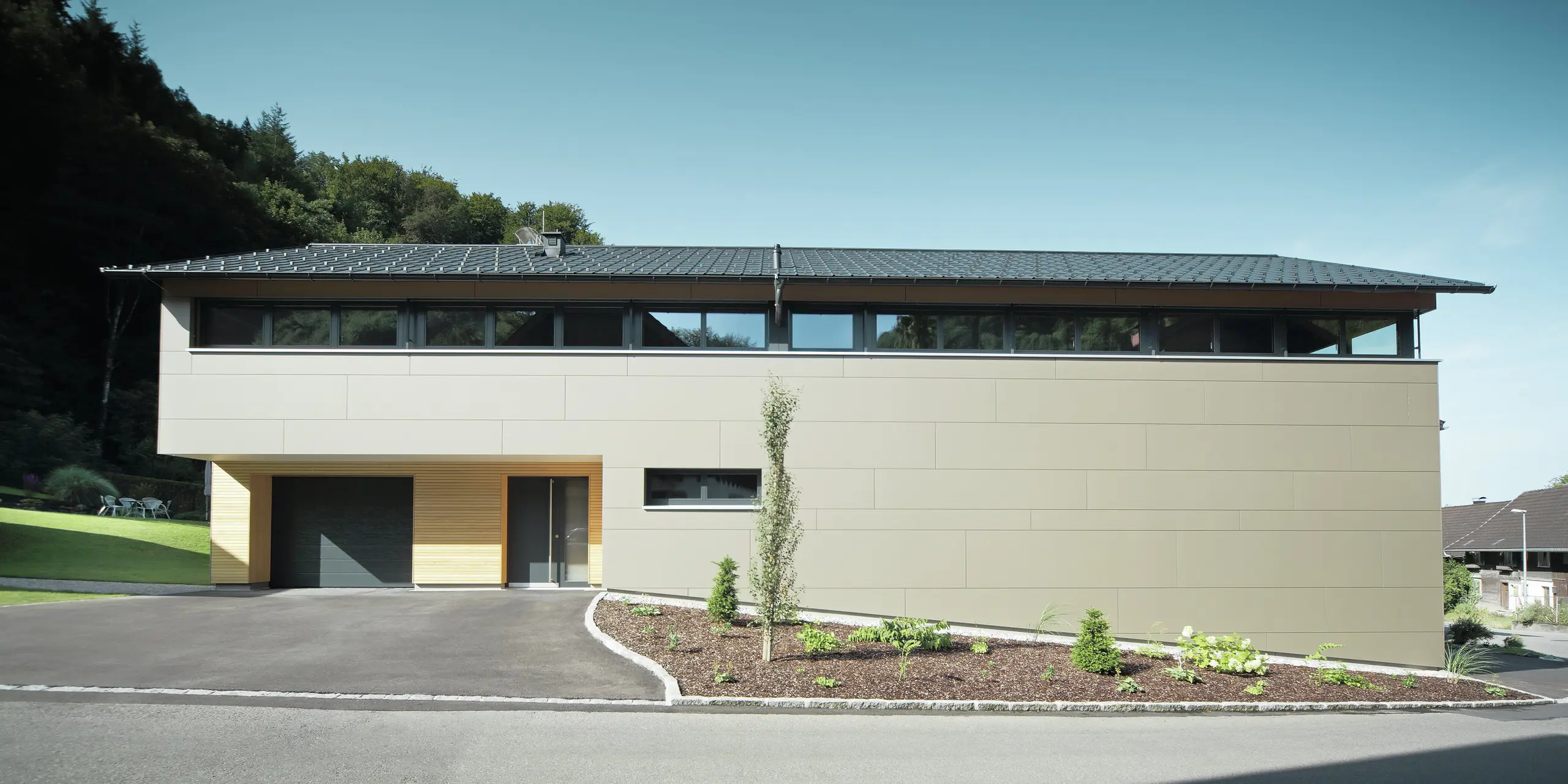 Hus med PREFA takpanel i P.10 antrasitt, kombinert med PREFA komposittpanel i bronse på fasaden; moderne byggestil kombinert med smale vinduer og trefasade.