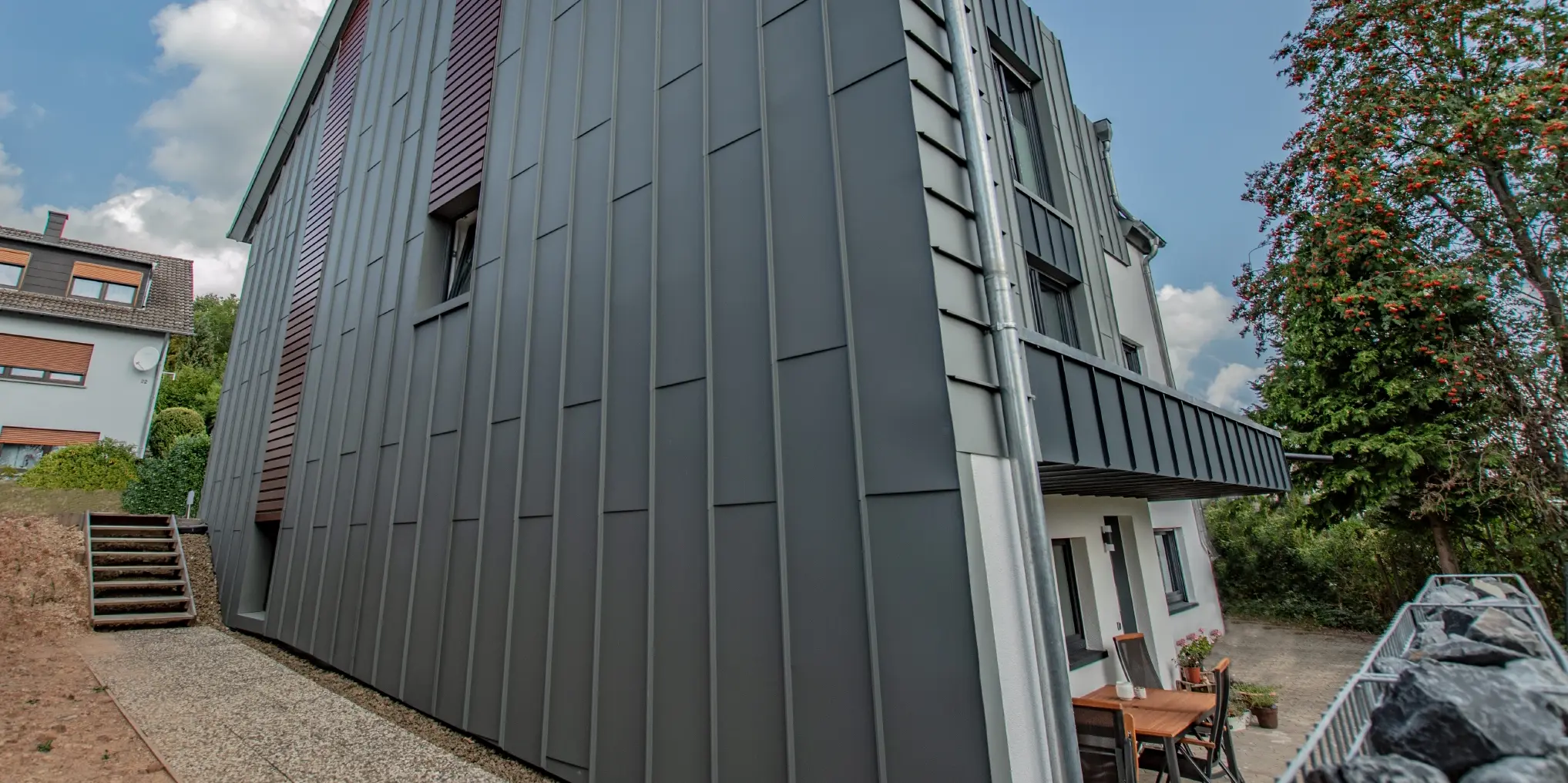 Fasadeutforming med vertikal vinkelståfalsfasade i lysegrå og fasadepaneler, montert horisontalt, i mørkt tre. Hele fasaden er utført i aluminium fra PREFA.