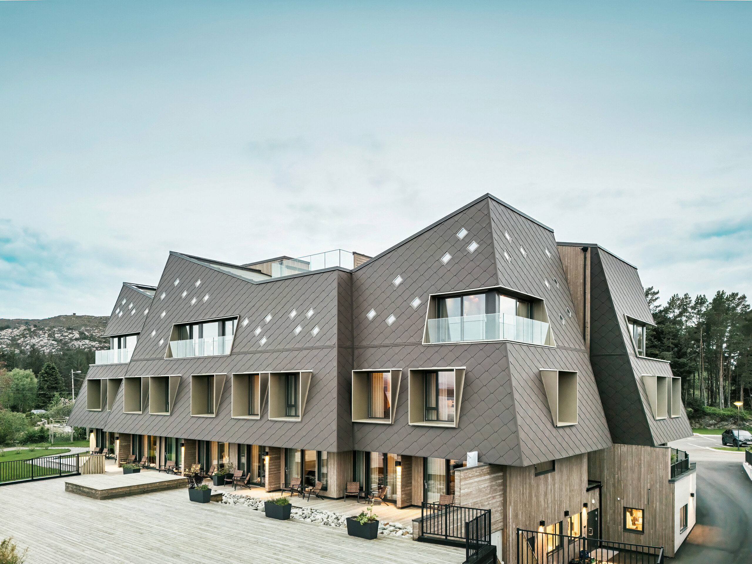 Utsikt over terrassen på hotellet Beckerwyc House i Bekkjarvik, Norge. Den moderne bygningen er utsmykket med en iøynefallende aluminiumsfasade laget av PREFA-veggribber 44 × 44 i valnøttbrun. Den futuristiske arkitekturen med skrånende takflater og utstikkende vinduselementer kompletteres av de romslige uteområdene. Fasadens naturlige farge passer harmonisk inn i det omkringliggende landskapet og understreker bygningens moderne design.