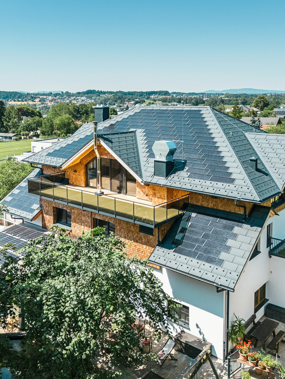 Vogelperspektive auf die Zenz'n Stub'n in Schörfling am Attersee mit neu saniertem Dach aus PREFA Solardachplatten und Dachplatten R.16 in P.10 Anthrazit. Das hochwertige Blechdach verbindet modernes Design mit nachhaltiger Energiegewinnung. Der großzügige Balkon und die harmonisch integrierte Dachentwässerung unterstreichen das stilvolle Erscheinungsbild des Gebäudes.