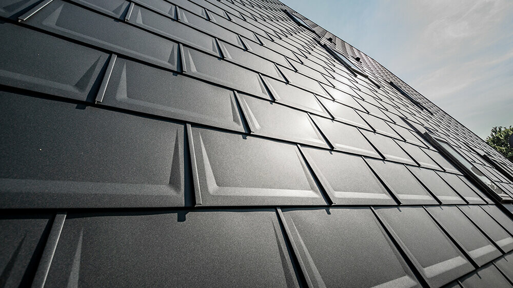 PREFA Dachplatte R.16 in Anthrazit ohne Schneeschutz mit schräg einfallender Sonne. Blechdach von PREFA.