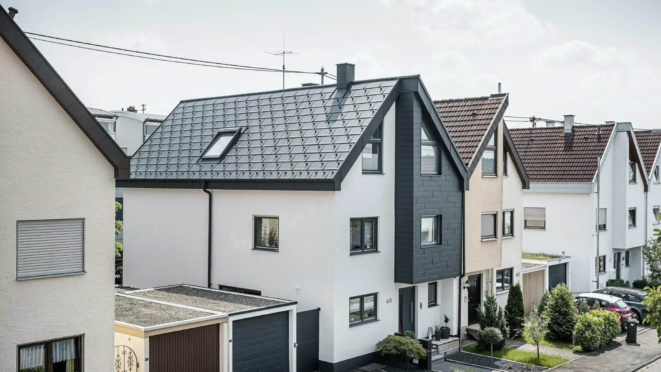 En tomannsbolig er allerede renovert, med en frisk fasade i hvit puss kombinert med en PREFA Siding.X-fasade i antrasitt. Taket ble dekket med PREFA R.16 takplate. Takdreneringen skjer via firkantrenne og PREFA nedløpsrør.