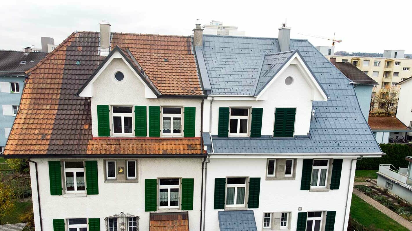 To hushalvdeler i Sveits: Den venstre delen av bygningen er ennå ikke renovert og er fortsatt dekket av flekkete takstein. Den høyre delen av bygningen er dekket med PREFA takplater i steingrått.
